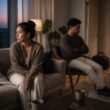 Two adults sit apart in a quiet living room after an emotional conversation, with one appearing withdrawn and the other reflective.