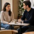 A reserved woman meets a supportive man in a quiet café, sitting with respectful distance and calm body language.