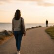 A person walks confidently along a sunlit path away from another distant figure.