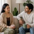 A reserved woman and her partner sit calmly together, with the partner listening attentively in a comfortable living room.